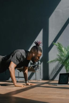 An adult man doing push-ups indoors, guided by a laptop. Fitness and technology merge.