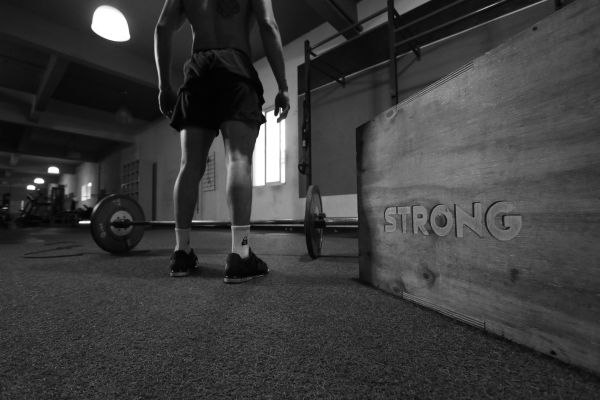 Black and white photo of a man in a gym with barbell and 'Strong' box.