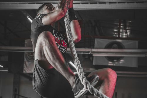 A determined man climbing a rope in an indoor gym setting, showcasing strength and fitness.