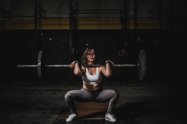A strong female weightlifter squats with a barbell in a dimly lit gym, showcasing power and fitness.